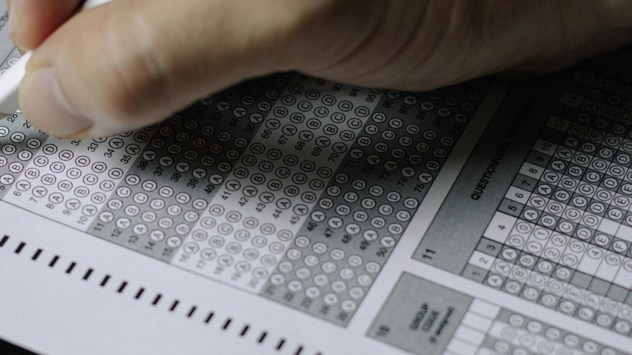 Une main remplit au crayon une feuille de réponses à cocher